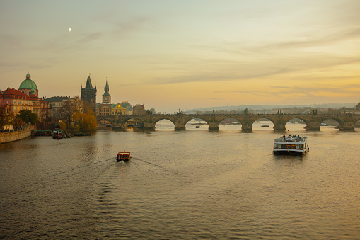 landscape with Vltava river, Charles Bridge and boat at sundown in autumn in Prague, Czech Republic.