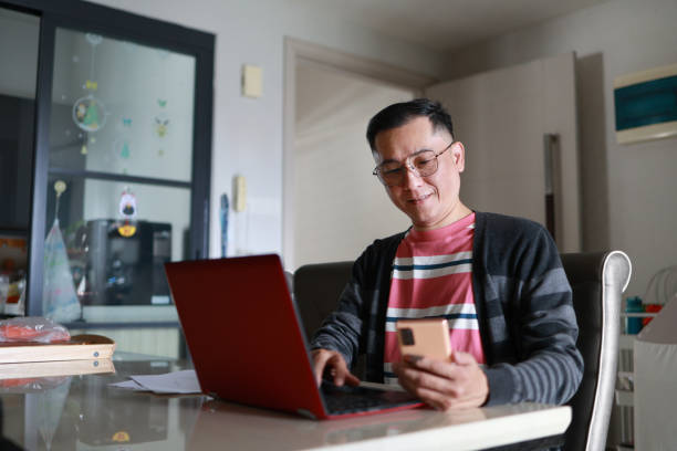 istock A confident Asian man is sitting at his home desk, using his laptop computer while also looking at his smartphone. 1620954380