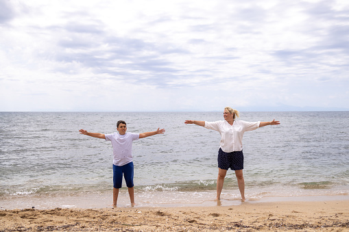 Front view of active and healthy Caucasian mother with her son, exercising on the beach,d during their vacation