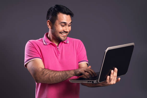 ritratto di brasiliano che indossa la polo rosa, guardando il suo taccuino, eccitato, tenendo il portatile con la mano sinistra e digitando con l'altra mano, sorridente - belém - pará - brasile - polo shirt flash foto e immagini stock