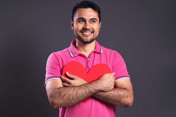 portrait of a brazilian wearing a pink polo shirt, hugging a red paper heart, looking to the side and smiling - belém - pará - brazil - human heart flash imagens e fotografias de stock