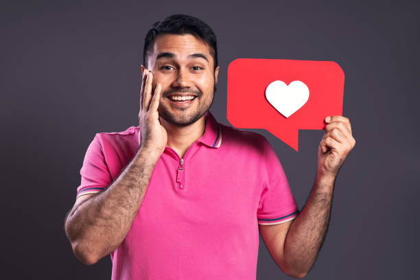 portrait of a brazilian wearing a pink polo shirt, holding with his left hand a speech bubble with a white heart inside, with his right hand on his face, happy, looking at the camera and smiling - belém - pará - brazil - human heart flash imagens e fotografias de stock