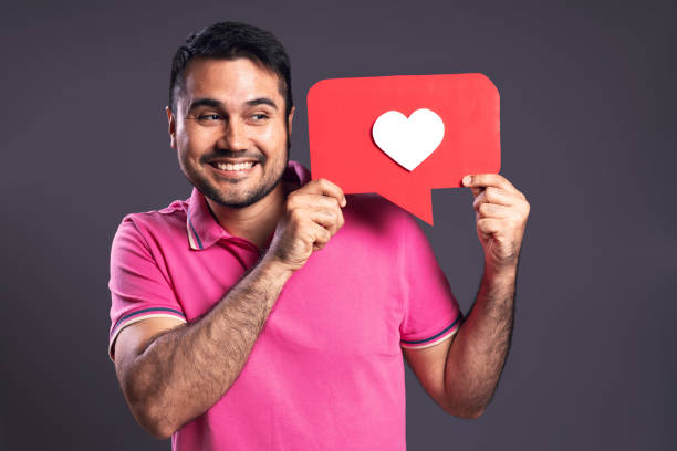portrait of a brazilian wearing a pink polo shirt, holding a speech bubble with a white heart inside with both hands, happy, looking to the side and smiling - belém - pará - brazil - human heart flash imagens e fotografias de stock