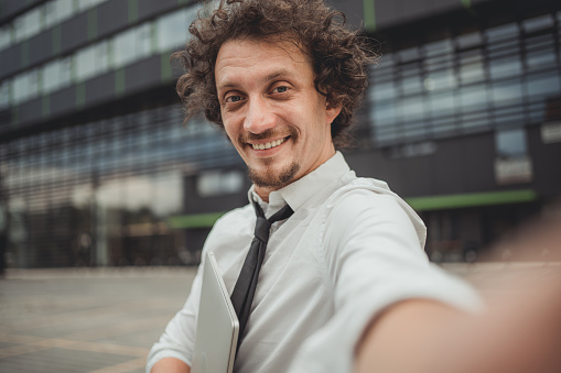 Portrait of happy young man in white shirt with tie looking at camera outdoors. A successful businessman in a city street.