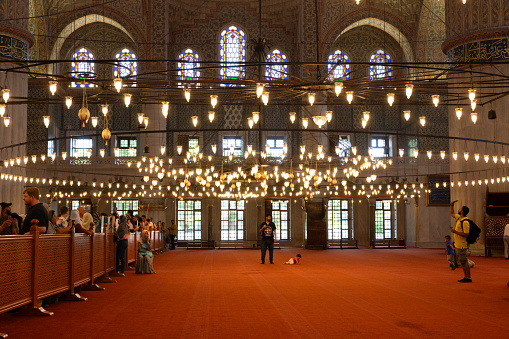 Interior of the Blue Mosque (Sultan Ahmet Mosque) and tourists - Archs and chandeliers - Istanbul, Turkey