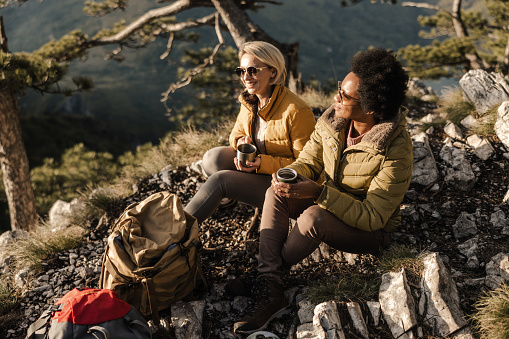 Two women taking a tea break during a hike in the mountains in a beautiful sunny autumn day.