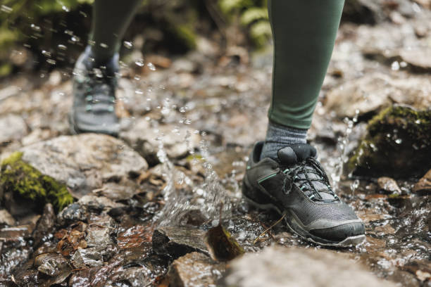A Latino adult man has his gray leather boots in the creek to cool off after having walked in the forest for a few good hours, this man is dressed in gray pants.