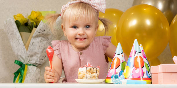 bambina bionda di due anni che mangia la torta di compleanno per il suo compleanno. - hat toddler little girls pink foto e immagini stock