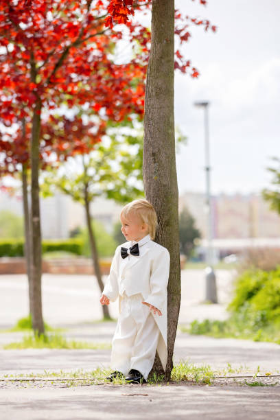 hermoso niño pequeño en esmoquin, jugando en un parque en un día de la boda - single lane road footpath flower formal garden fotografías e imágenes de stock