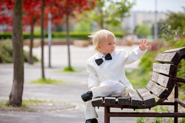 hermoso niño pequeño en esmoquin, jugando en un parque en un día de la boda - single lane road footpath flower formal garden fotografías e imágenes de stock