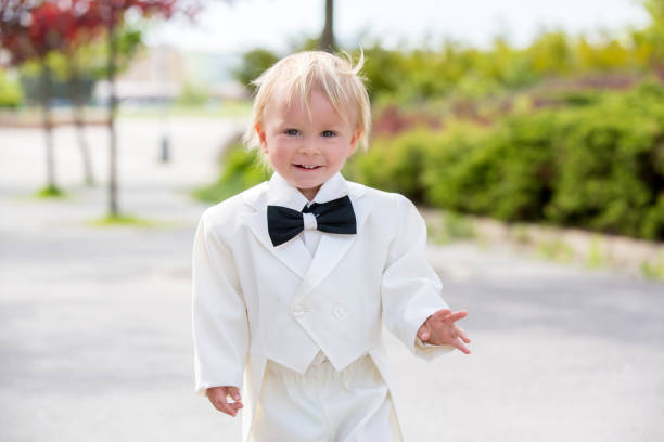 hermoso niño pequeño en esmoquin, jugando en un parque en un día de la boda - single lane road footpath flower formal garden fotografías e imágenes de stock