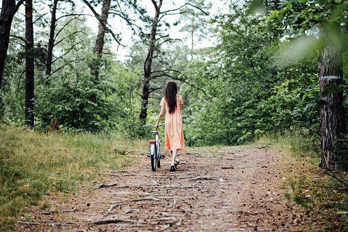 Walk in the woods for wellness, Health benefits of forests. Immerse Yourself in a Forest. A young girl rolls a bicycle along a forest path in tree wood.
