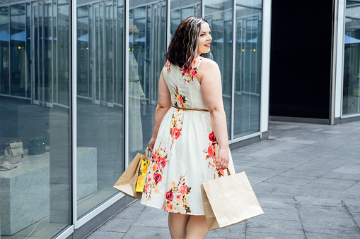 How to Shop for Summer Fashion on a Budget. Choosing the Right Fabrics for Hot and Humid Summer Weather. Outdoor portrait of stylish curvy woman with shopping bags.