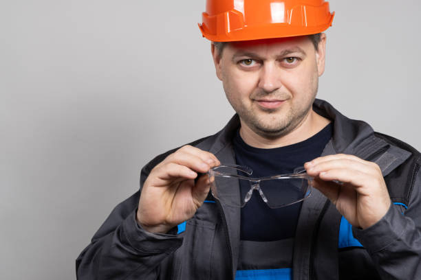 istock A construction worker in a helmet and overalls put on goggles protective glasses on a white background. 1621079923