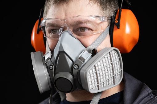 Portrait of a man wearing a respirator and protective noise-cancelling headphones earmuffs.