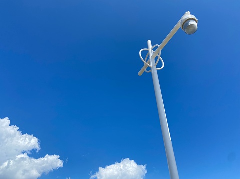 Looking up at the clear blue sky framed by fluffy white clouds and a white retro lamppost on the boardwalk on a summer day in the Rockaways, Queens, New York City
