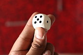A dice facing 5 or five in the hand of a guy with red blurred Background