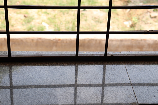 A window made up of iron bars with reflection of it on the marble below it