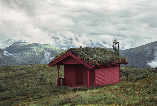 Red hut in the mountains with green grass and clouds in Norway