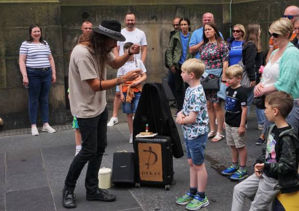Edinburgh, Scotland - 14 August 2023: A street magician has enlisted the help of a young assistant to help entertain a small crowd during the Edinburgh Fringe. Taken in the historic High Street.