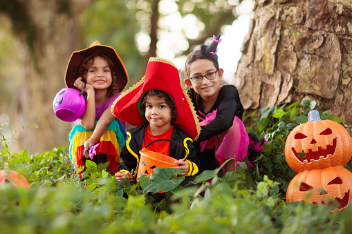 Child in Halloween costume. Mixed race kids and parents trick or treat on street. Little boy and girl with pumpkin lantern and candy bucket. Baby in witch hat. Autumn holiday fun.