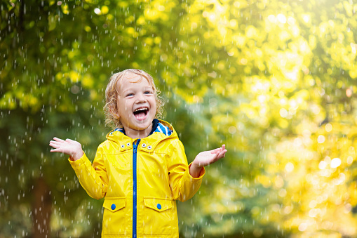 Kids play in autumn rain. Child playing outdoor on rainy day. Little boy catching rain drops under heavy shower. Fall storm in a park. Waterproof wear for kid. Children outdoors by any weather.