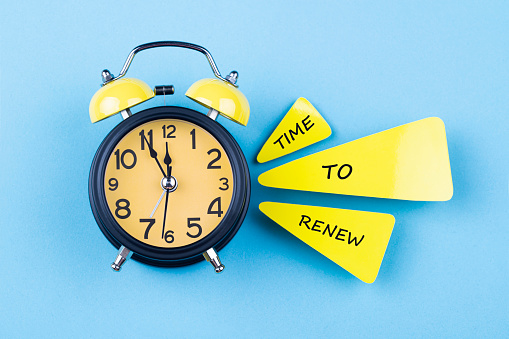 Alarm clock and papers with text Time to renew, on blue background. The clocks time is showing 5 to 12.