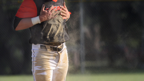 Closeup of a baseball player brushing dirt off of his uniform with room for copy on the right side of the frame.
