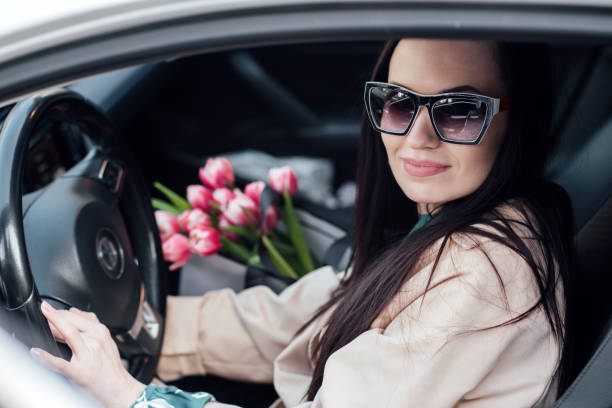 istock Female-centric car customization. Designing cars specifically to women's needs and preferences. Female-focused car safety features. A woman with bouquet of tulips flowers gets into the car 1621166540