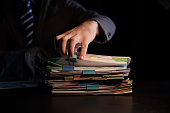 Business Employee hand working in Stacks paper files for searching and check unfinished document archives on folders papers at busy work desk workplace office.