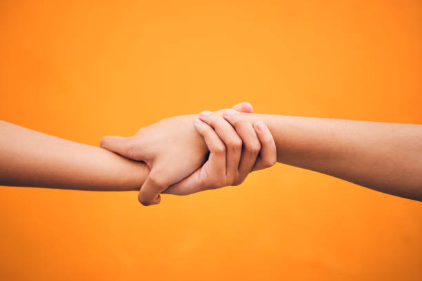 Holding hands, studio and closeup for support, help and care for teamwork by orange background. People, friends and together for solidarity, link and connection with synergy, partnership and strong