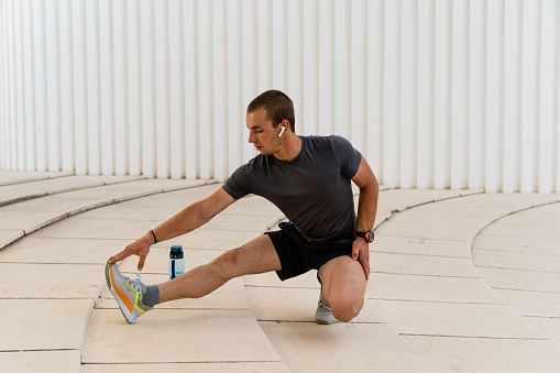A young man stretching his legs and arms while doing exercise outdoors