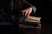 Business Employee hand working in Stacks paper files for searching and check unfinished document archives on folders papers at busy work desk workplace office.