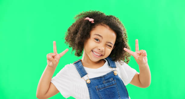 istock Face, smile and child with peace sign on green screen in studio isolated on a background. Portrait, emoji and wink of happy kid or girl with v hand gesture or symbol for happiness or joy. 1621199956
