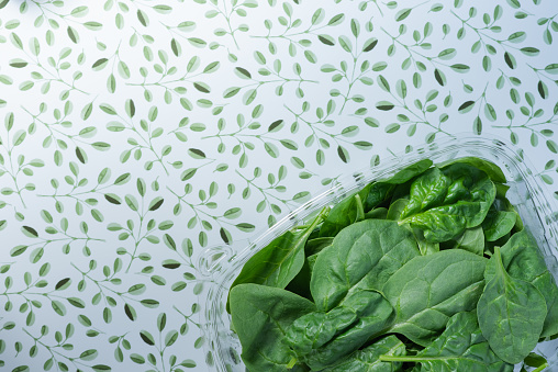Clear, plastic container holding fresh spinach.  Small, green leaf and white background.