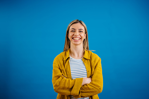 Portrait of a happy young woman standing in front of a blue background.