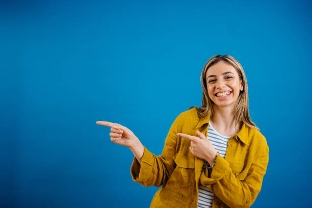 istock Happy Young Woman Pointing While Standing Against A Blue Background 1621203152