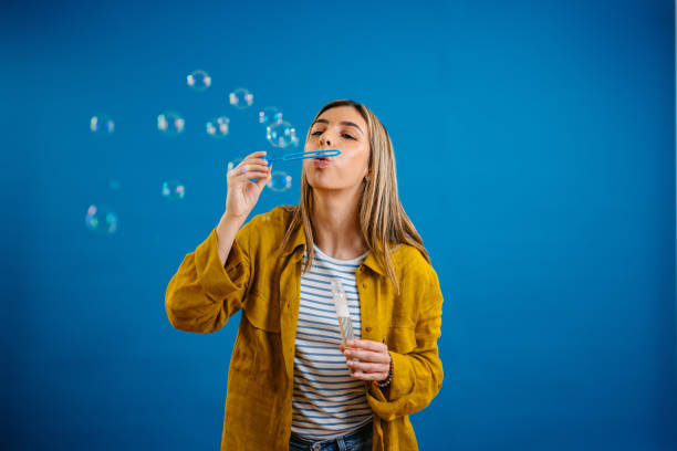 istock Young Woman Blowing Bubbles Against A Blue Background 1621207532