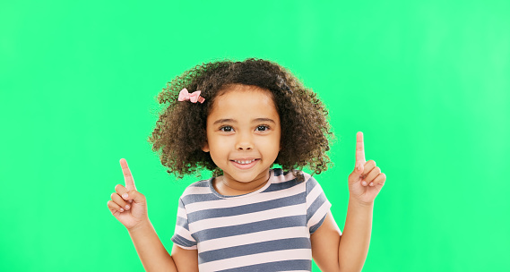 Face smile, girl child and pointing up on green screen in studio isolated on a background. Portrait, emoji and happy kid with hand gesture for mockup, advertising or marketing, branding or chroma key