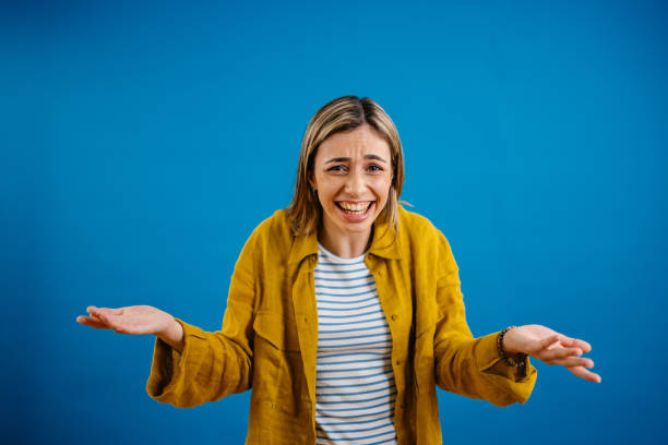 Young Woman Shrugging Her Shoulders While Standing Against A Blue Background