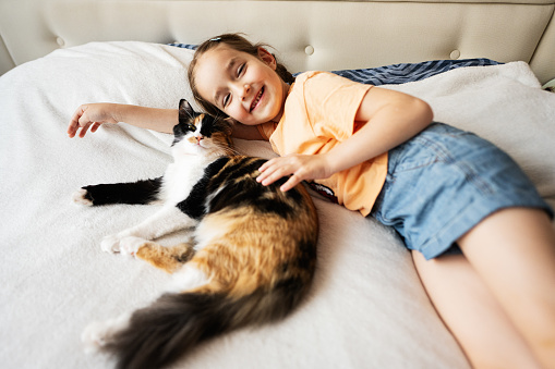 Cute little girl lying on the bed with her cat at home