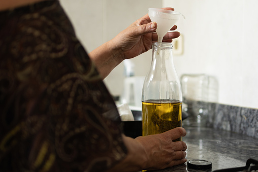 woman in the kitchen at home filling a glass bottle with used olive oil for cooking.recycling concept,zero waste in the water and sustainability and environment.