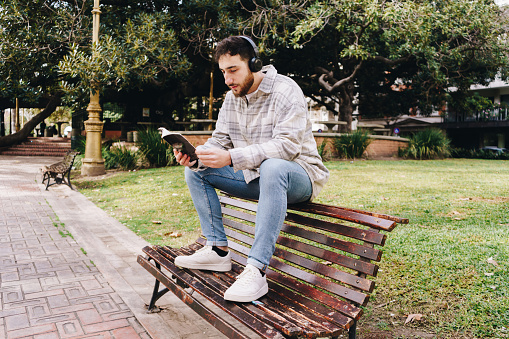 Mid adult man reading a book and listening music outdoors