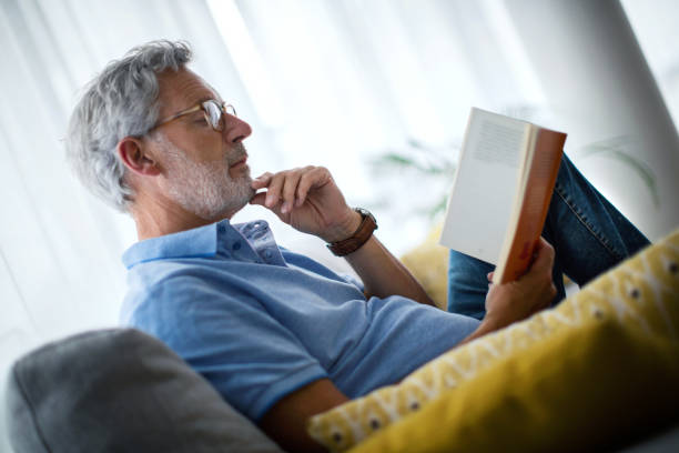 istock Mature man reading a book on the sofa. 1621219211