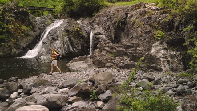 Female backpacker walking on the rocks by the waterfall in nature.