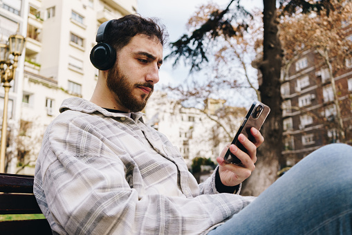 Mid adult man using mobile phone and listening music outdoors