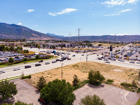 An aerial vantage unveils the expansive suburbs of Salt Lake City—neighborhoods budding, roads pulsing, and shopping areas thriving. Mountainous horizons lend a majestic backdrop as subdivisions bloom with greenery.