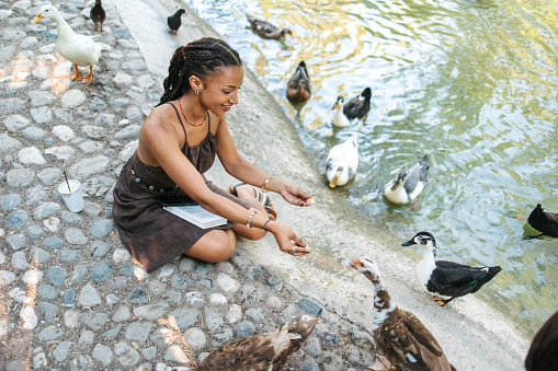 An African woman feeding birds by the lake. She came to read but birds interrupted her