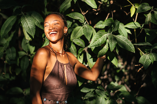 A young multi-racial woman smiling in the forest in front of a plant with big green leaves. Playing with sunlight and shadows