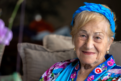 Happy, smile and portrait of a senior woman relaxing in the room of her retirement home. Happiness, excited and elderly female person with a positive mindset sitting in the living room of her house.